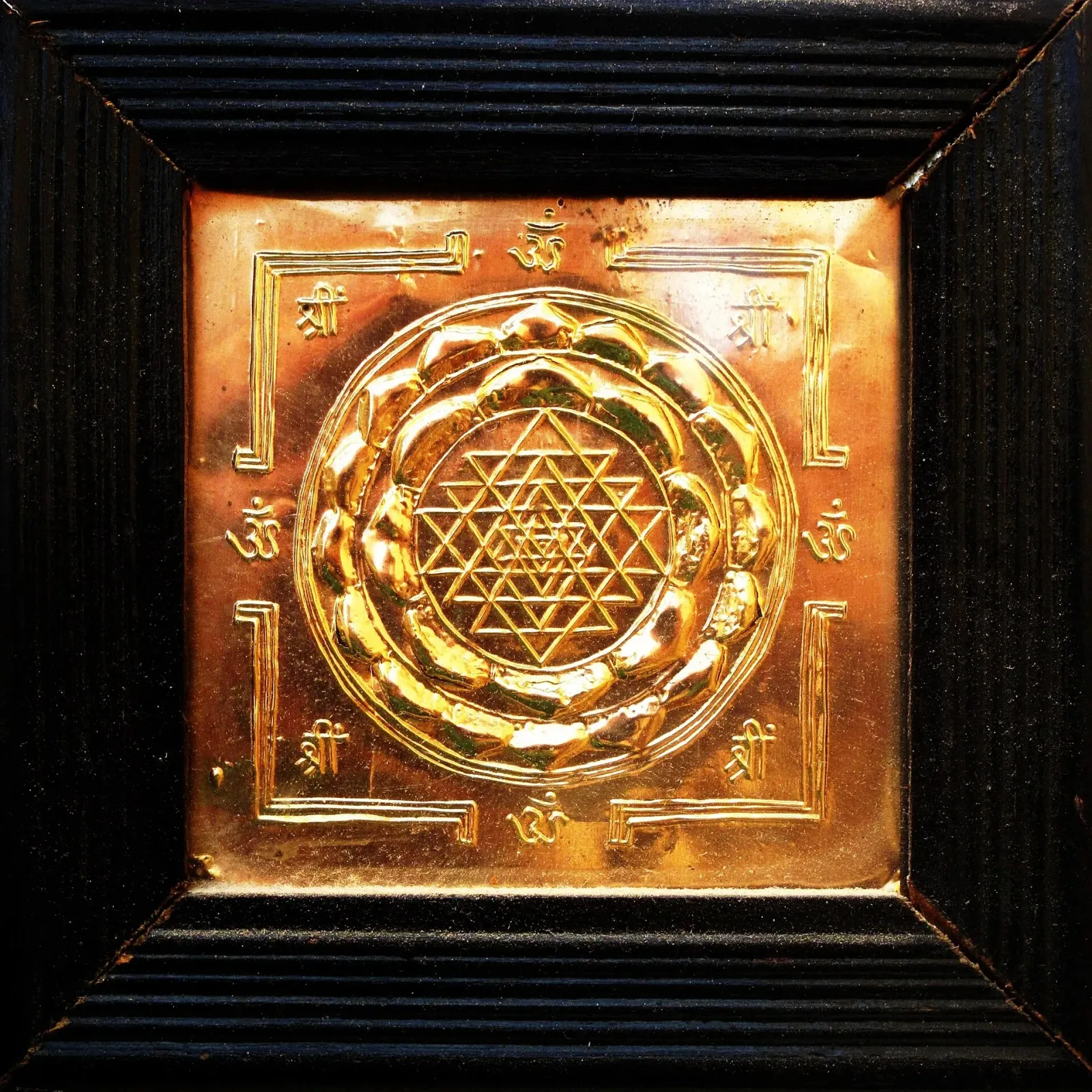 A Sri Yantra embossed in copper: nine interlocking triangles inside lotus petals and a square gated enclosure.